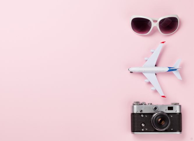 A pair of sunglasses, a toy plane, and camera on a light pink background.